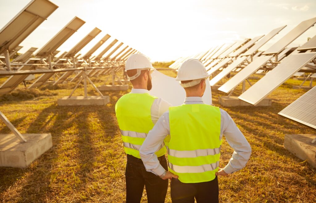 Unrecognizable contactors reading blueprint on solar farm in evening